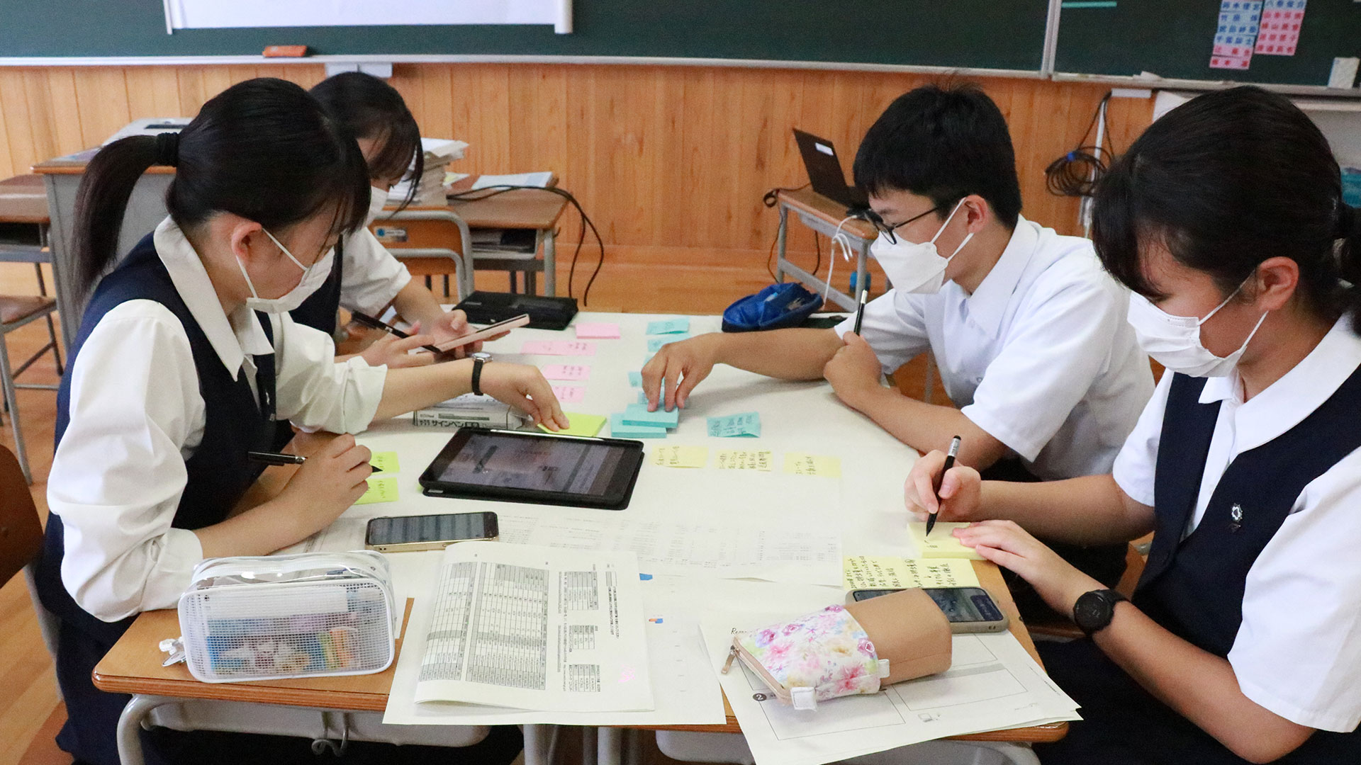 机に広げた模造紙に、意見を書いた付箋を貼り付けていく高校生たち