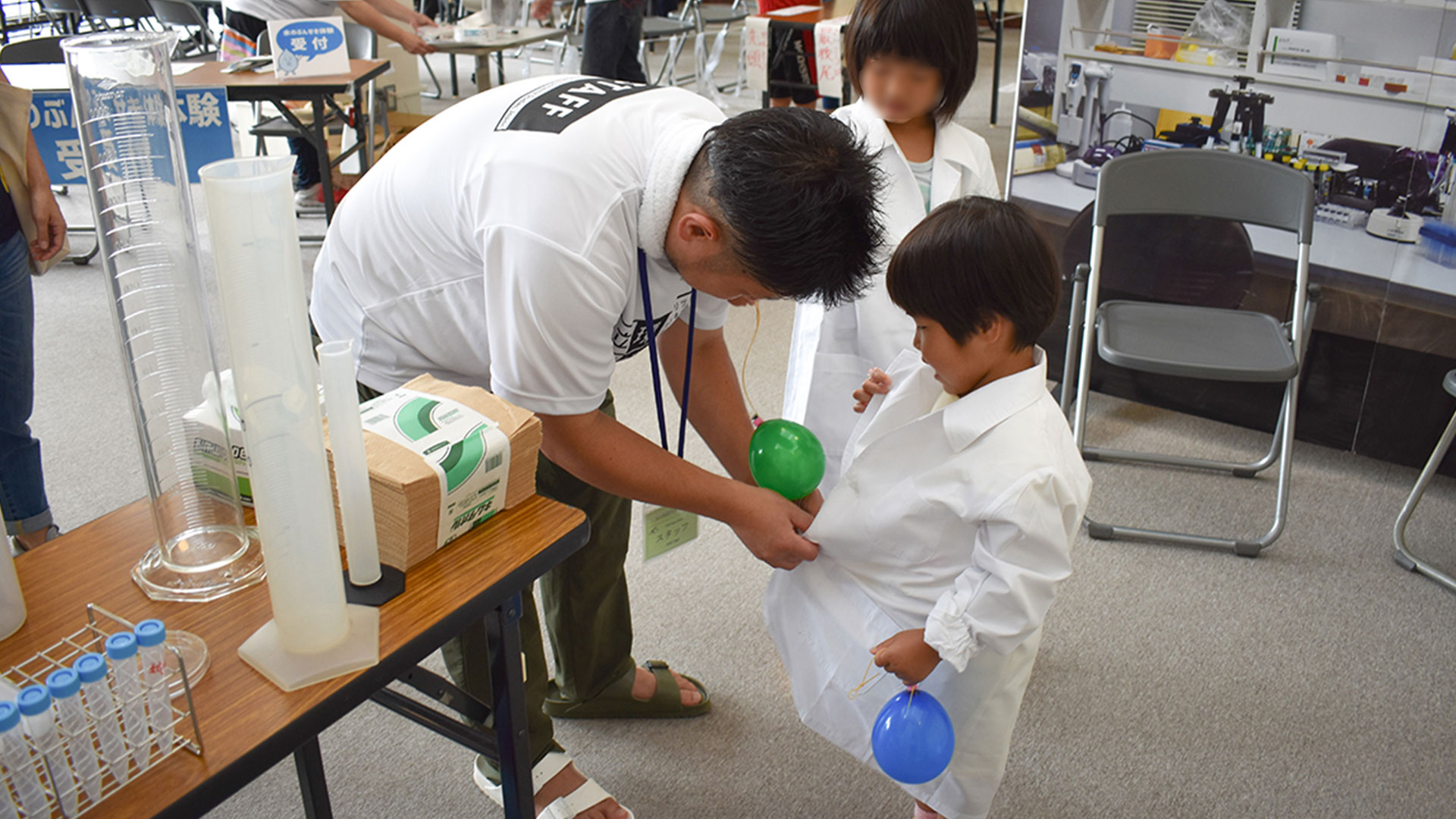 来場者のお子さんに白衣を着せる渡邊さん